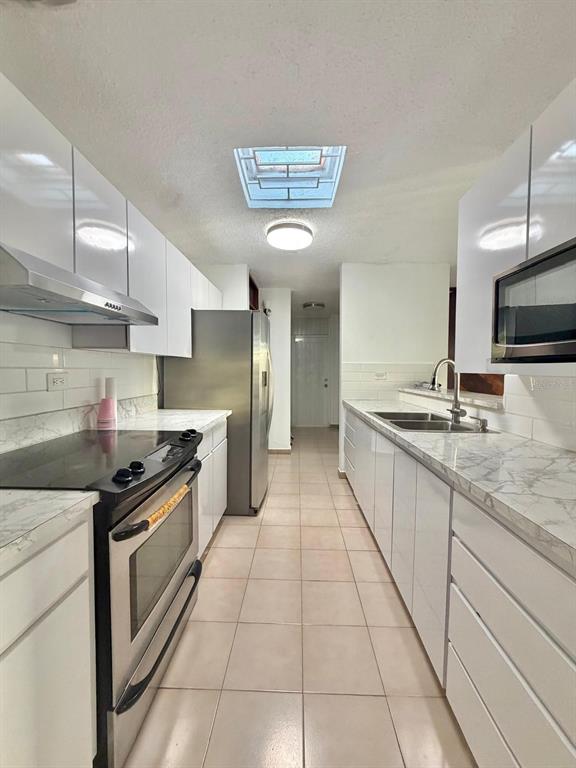 A galley kitchen features white cabinets, marble-look countertops, stainless steel appliances, and a skylight — 2105 CALLE ANTIOQUIA, GUAYNABO, PR