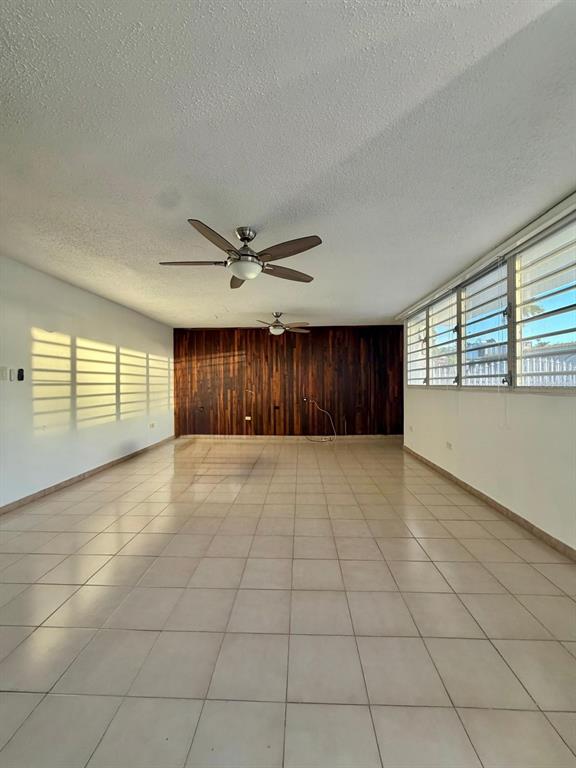 A spacious, empty room features light-colored tile floors, a wood-paneled accent wall, and ceiling fans — 2105 CALLE ANTIOQUIA, GUAYNABO, PR