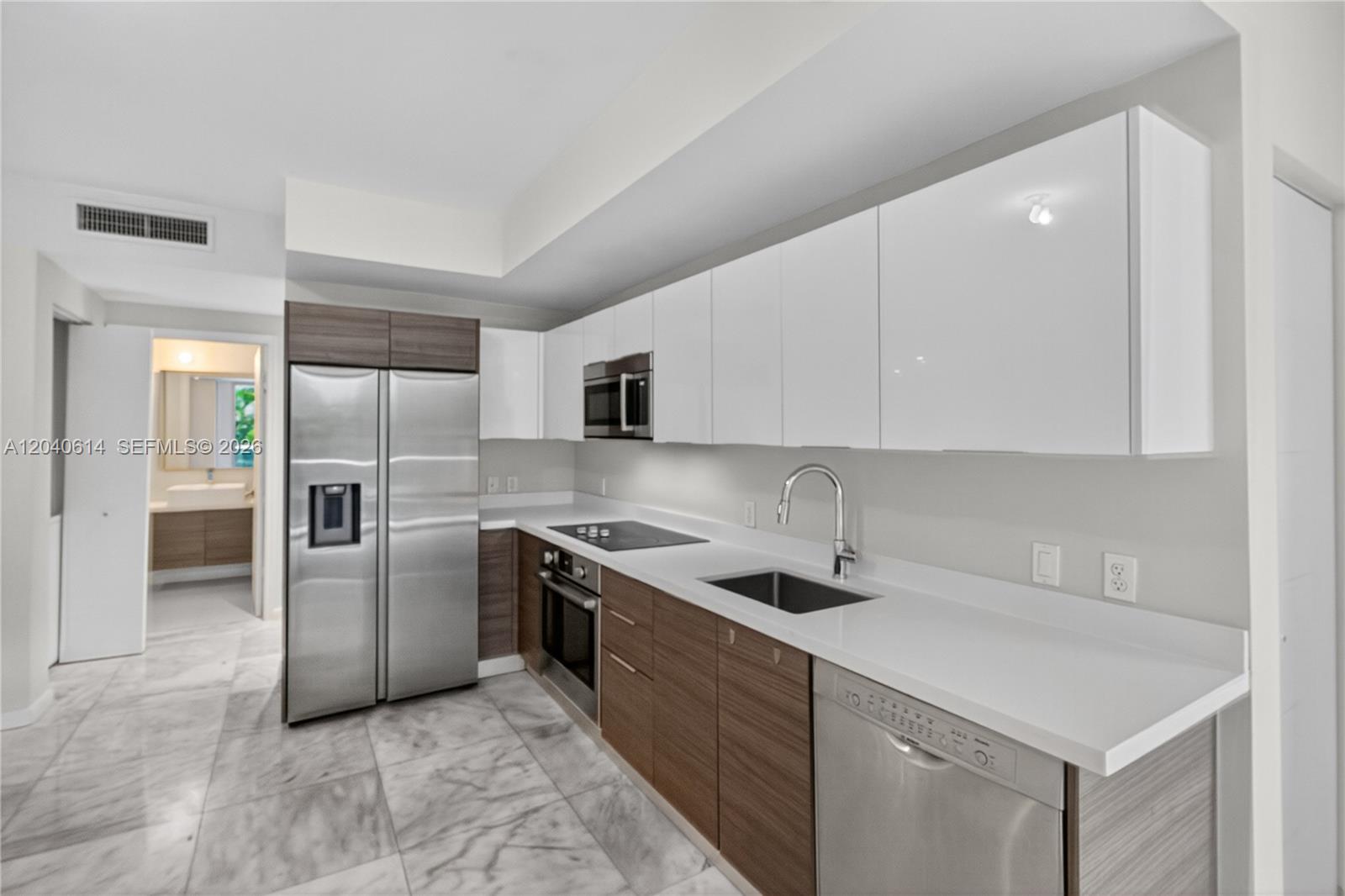 A modern kitchen features white upper cabinets, wood-tone lower cabinets, stainless steel appliances, and marble flooring — 1010 SW 2nd Ave # 603, Miami FL 33130, MIAMI, FL