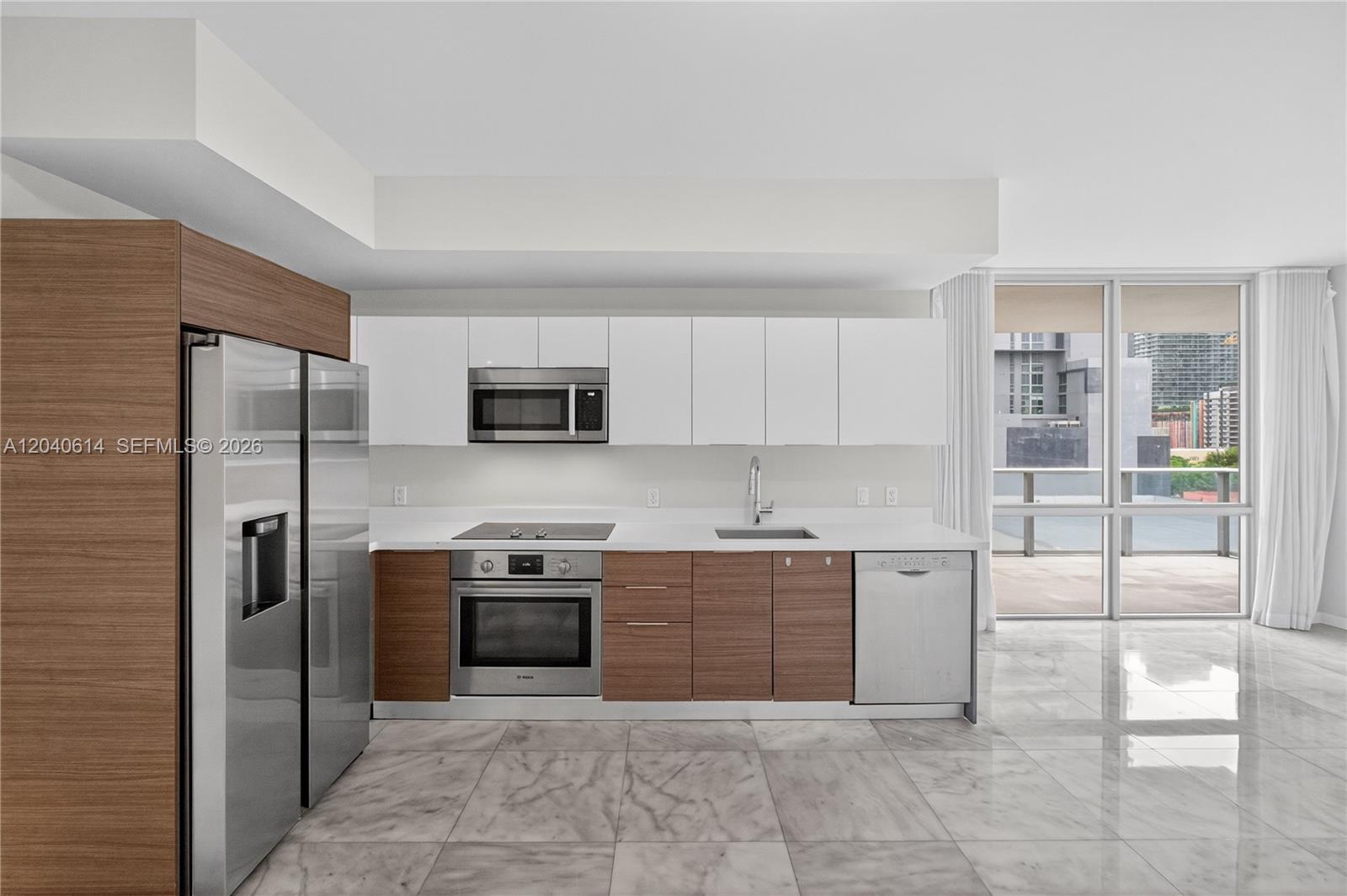 A modern kitchen features wood-tone lower cabinets, white upper cabinets, stainless steel appliances, and marble flooring — 1010 SW 2nd Ave # 603, Miami FL 33130, MIAMI, FL