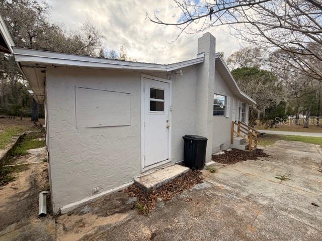 The exterior of a light-colored house features a white door, a chimney, and a driveway — 3294 E WAGON TRAIL, HERNANDO, FL