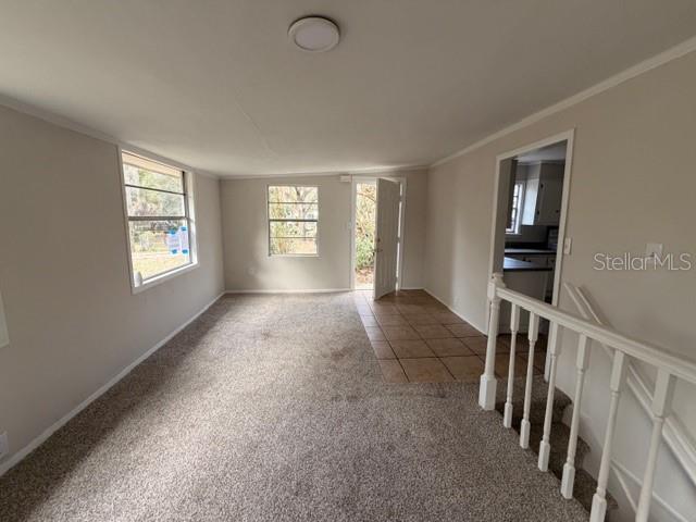 A carpeted living room features a tiled entryway, a white door, and a staircase railing — 3294 E WAGON TRAIL, HERNANDO, FL