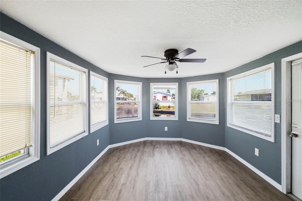 A sunroom with gray walls, wood-look flooring, a ceiling fan, and multiple windows overlooking water — 3300 COQUINA ESPLANADE, PUNTA GORDA, FL