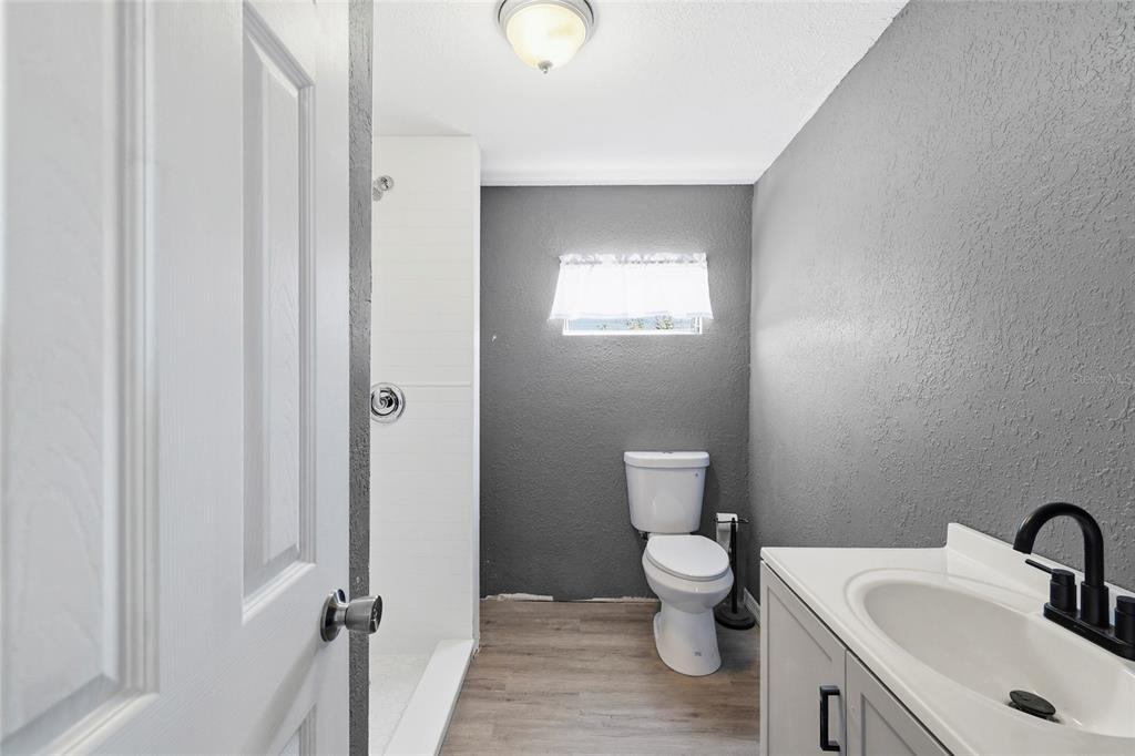 A bathroom features a white vanity, a toilet, and a walk-in shower with gray walls — 3300 COQUINA ESPLANADE, PUNTA GORDA, FL