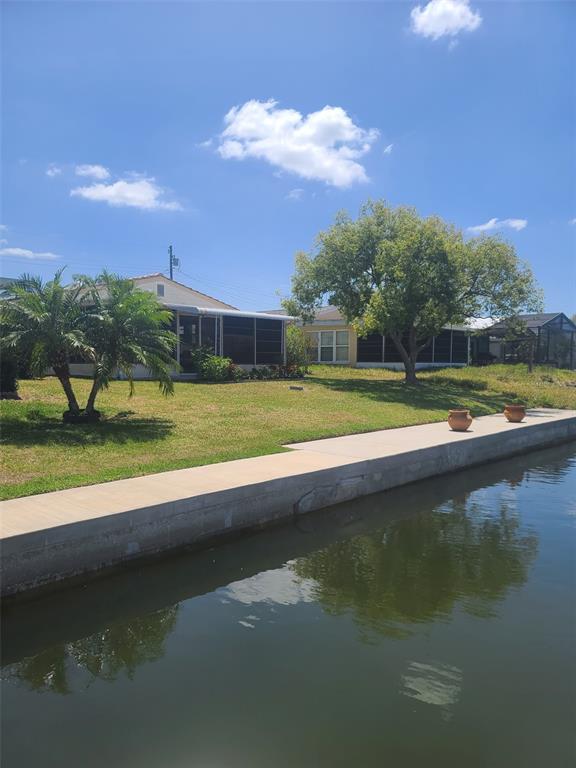 A view of a waterfront home with a concrete seawall, lawn, and two trees — 5105 BONITO DRIVE, NEW PORT RICHEY, FL