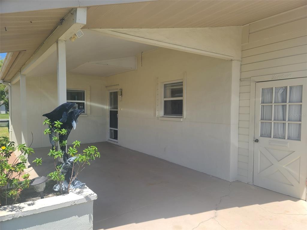 A covered concrete patio features a dolphin statue, two windows, and a white paneled door — 5105 BONITO DRIVE, NEW PORT RICHEY, FL