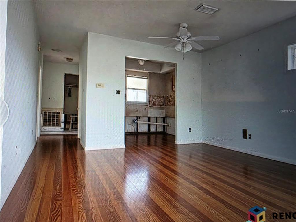 A living room with hardwood floors leads into an unfinished kitchen area with exposed plumbing — 5105 BONITO DRIVE, NEW PORT RICHEY, FL