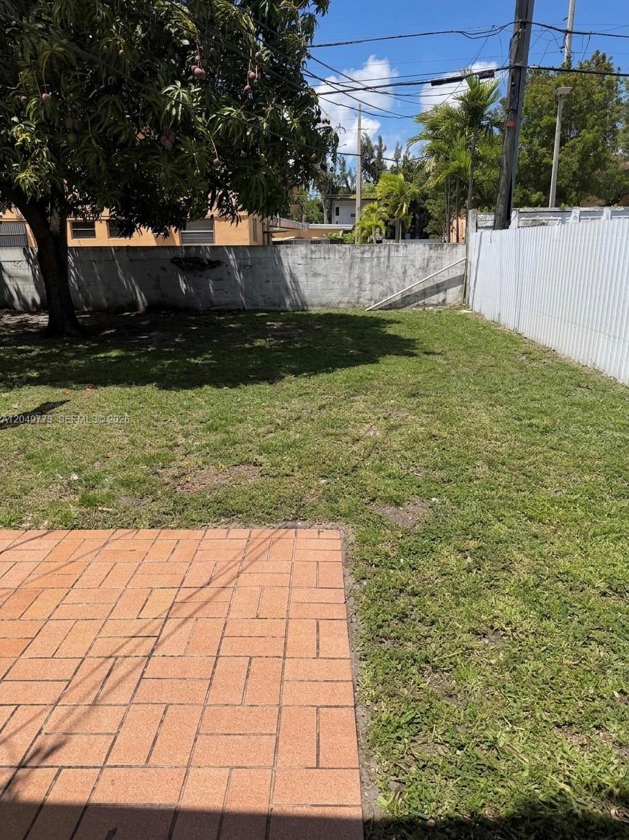 A backyard features a brick patio, a grassy lawn, a large tree, and a concrete wall — 41 E 20th St, Hialeah FL 33010, HIALEAH, FL