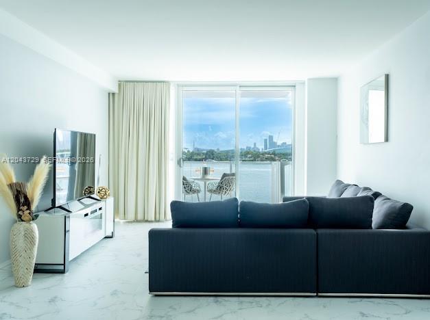 A living room with a dark sectional sofa, white media console, and balcony overlooking water — 1100 West Ave # 510, Miami Beach FL 33139, MIAMI BEACH, FL
