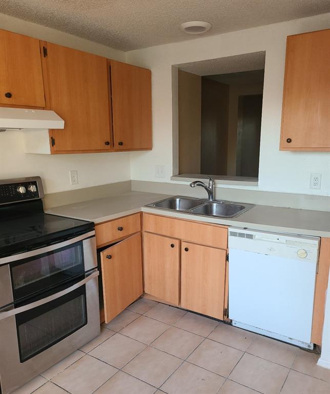 A kitchen features light wood cabinets, a stainless steel stove, and a white dishwasher — 4916 SILVER OAKS VLG UNIT E, ORLANDO, FL