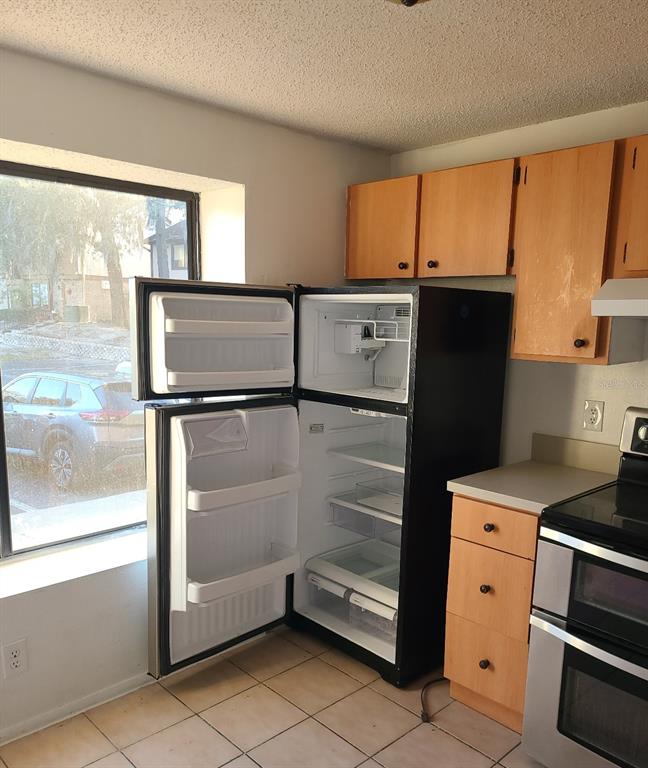 A kitchen with light wood cabinets, a black refrigerator with the door open, and tile flooring — 4916 SILVER OAKS VLG UNIT E, ORLANDO, FL