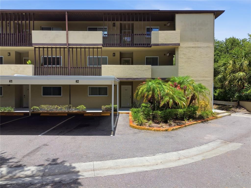 A multi-story apartment building features a covered parking area with numbered spaces and landscaping — 1247 S MARTIN LUTHER KING JR AVENUE UNIT 107, CLEARWATER, FL