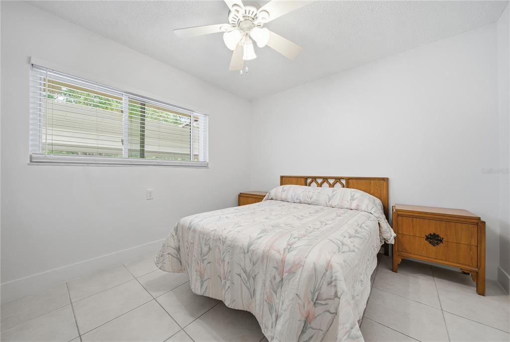 A bedroom with white walls, tile flooring, a ceiling fan, and a wooden bed frame — 1247 S MARTIN LUTHER KING JR AVENUE UNIT 107, CLEARWATER, FL