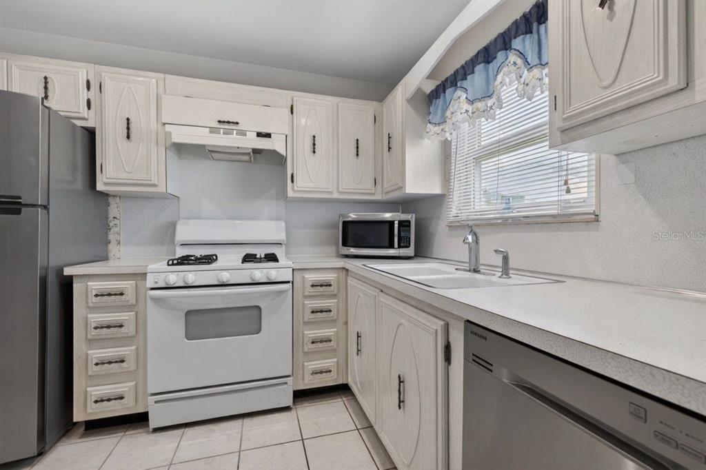 A kitchen with white cabinets, a white stove, a stainless steel dishwasher, and tiled floors — 5357 81ST STREET N UNIT 12, ST PETERSBURG, FL