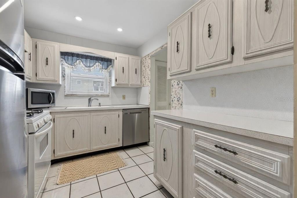 A kitchen with white cabinets, light countertops, stainless steel appliances, and white tiled flooring — 5357 81ST STREET N UNIT 12, ST PETERSBURG, FL