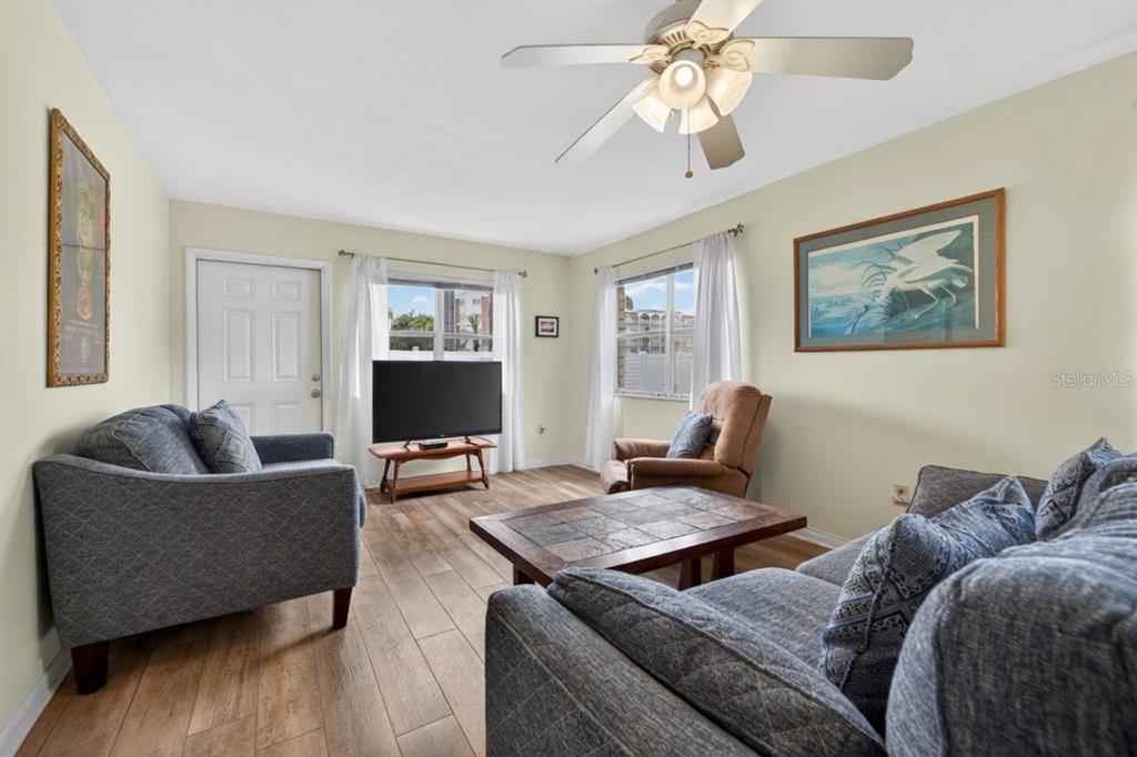 A living room features gray sofas, a brown armchair, a television, and wood-look flooring — 5357 81ST STREET N UNIT 12, ST PETERSBURG, FL