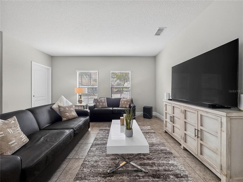 A living room features two black leather sofas, a white coffee table, and a large television — 127 KENNY BOULEVARD, HAINES CITY, FL