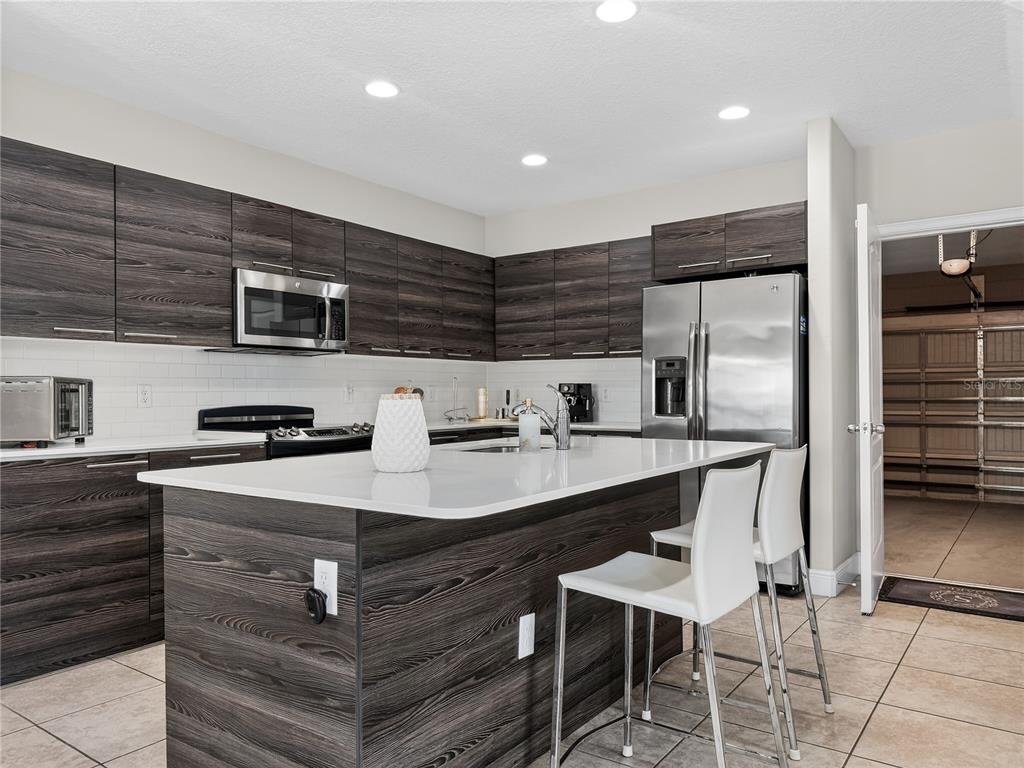 A modern kitchen features dark wood-grain cabinets, a white quartz island, and stainless steel appliances — 127 KENNY BOULEVARD, HAINES CITY, FL