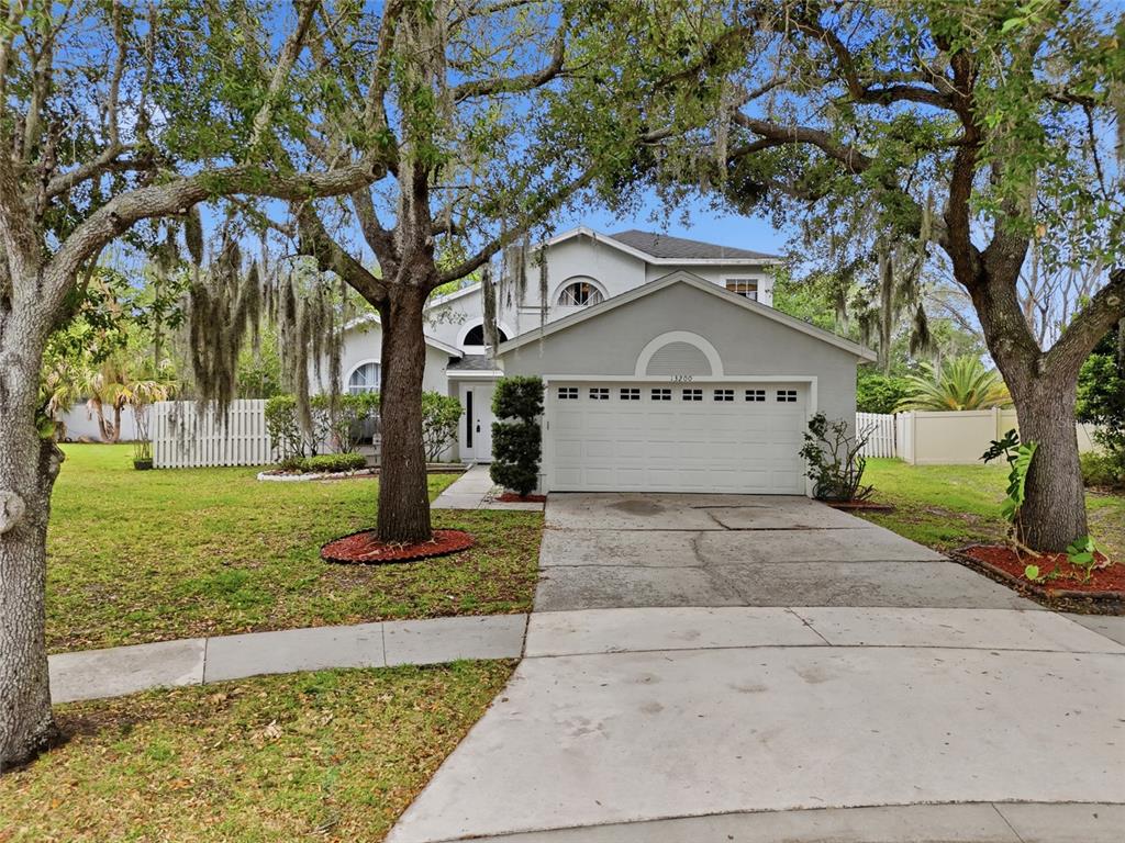 A two-story house with a white garage door, gray siding, and large trees in front — 13200 MALLARD COVE BOULEVARD, ORLANDO, FL