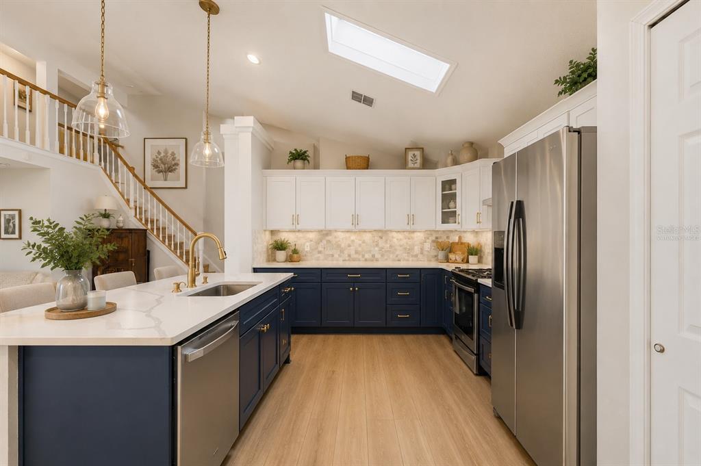A kitchen features white upper cabinets, navy lower cabinets, a quartz island, and stainless appliances — 13200 MALLARD COVE BOULEVARD, ORLANDO, FL