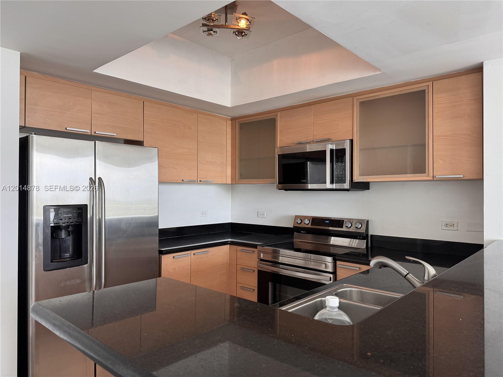 A kitchen features light wood cabinets, black countertops, stainless steel appliances, and a recessed ceiling — 140 S Dixie Hwy # 933, Hollywood FL 33020, HOLLYWOOD, FL