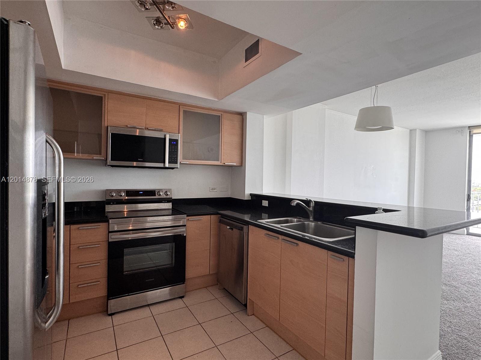 A kitchen features light wood cabinets, black countertops, stainless steel appliances, and tiled flooring — 140 S Dixie Hwy # 933, Hollywood FL 33020, HOLLYWOOD, FL
