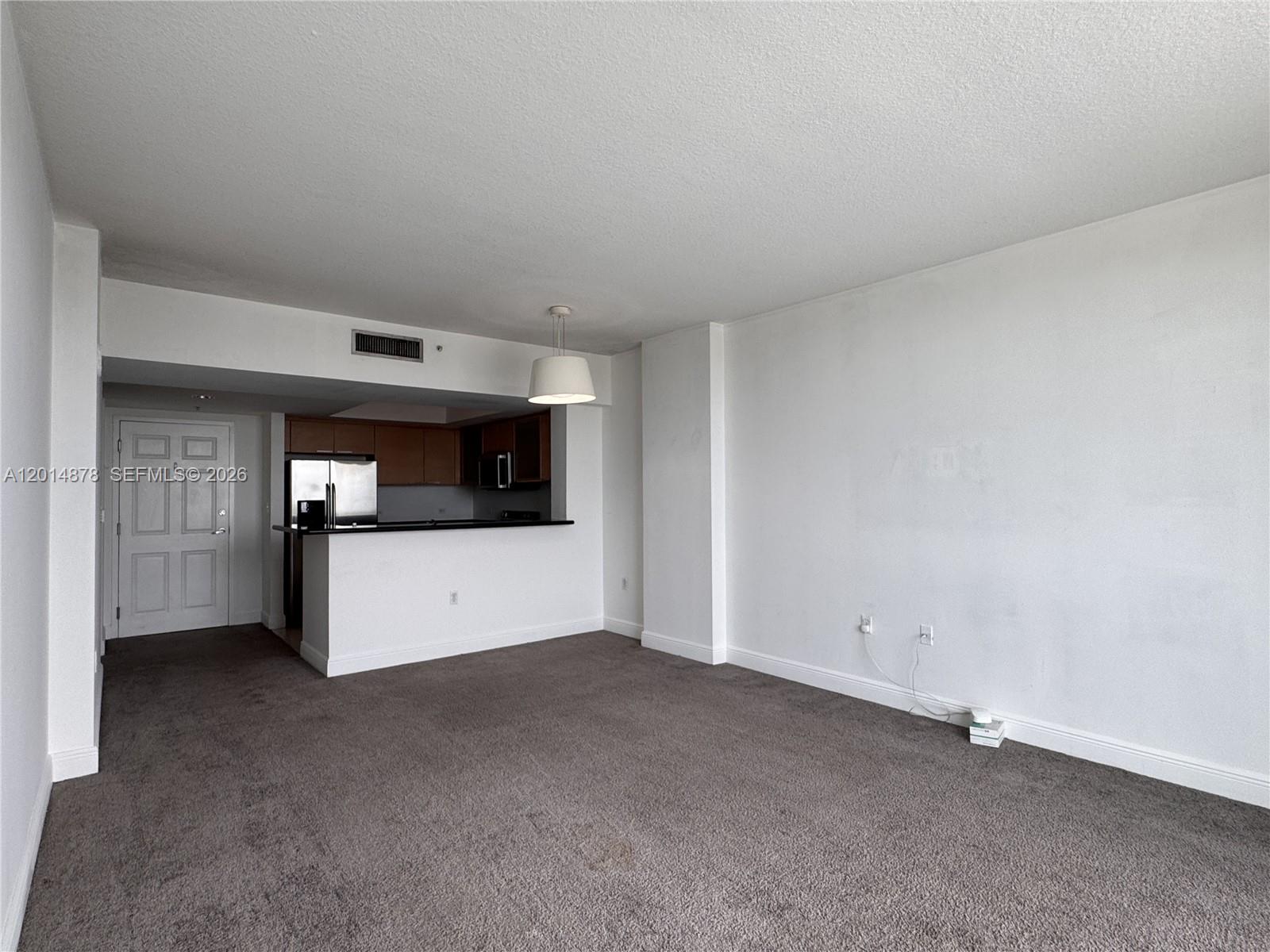 An unfurnished living room features gray carpeting, white walls, and an open kitchen area — 140 S Dixie Hwy # 933, Hollywood FL 33020, HOLLYWOOD, FL