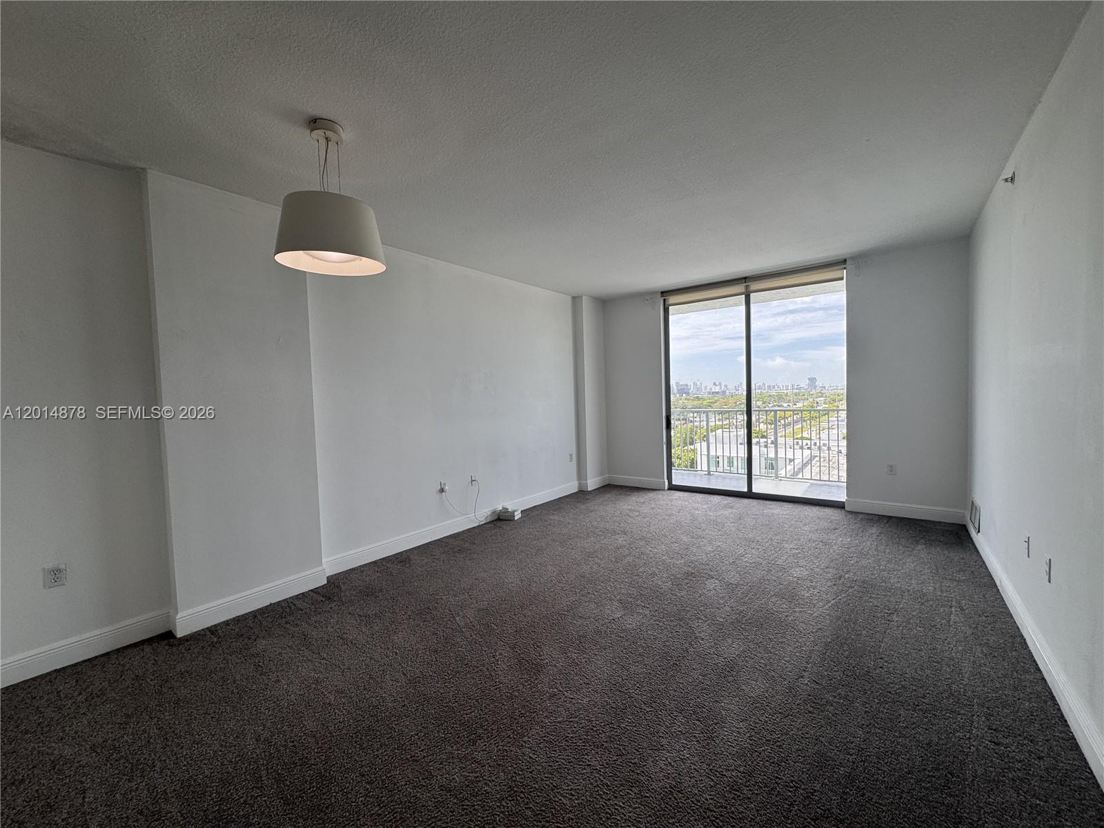 An empty living room features gray carpeting, white walls, a pendant light, and a balcony — 140 S Dixie Hwy # 933, Hollywood FL 33020, HOLLYWOOD, FL