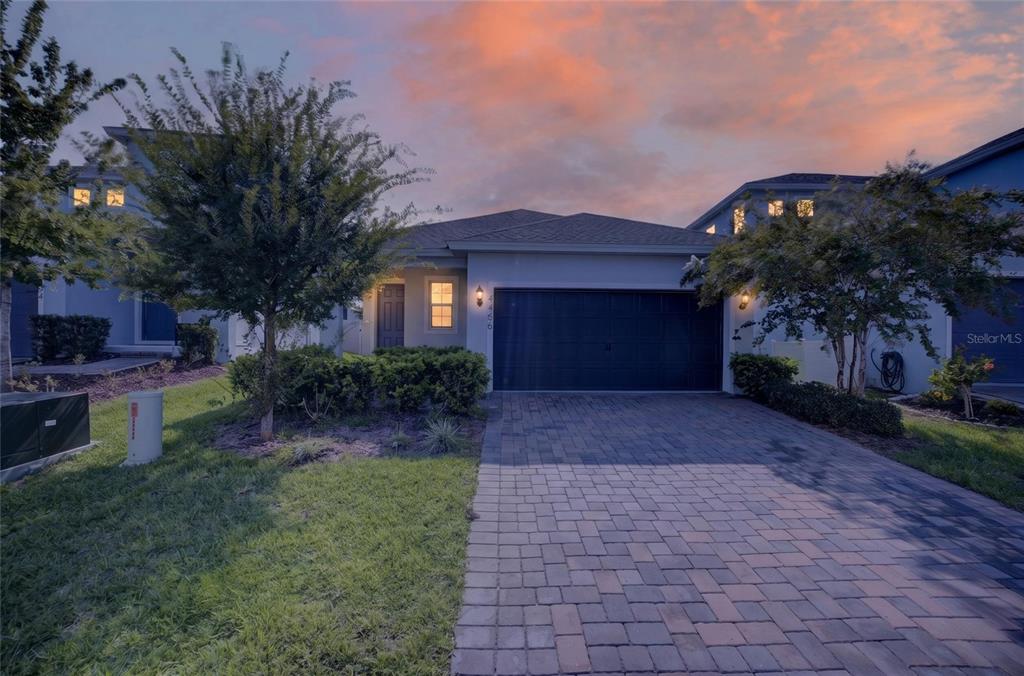 A single-story house with a paved driveway, dark garage door, and landscaping at dusk — 4406 DAVOS DR, CLERMONT, FL