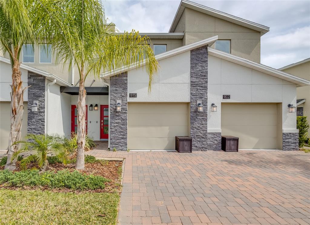 The exterior of two attached townhomes features stone accents, beige garage doors, and paved driveways — 815 OCEAN COURSE AVENUE UNIT 815, DAVENPORT, FL