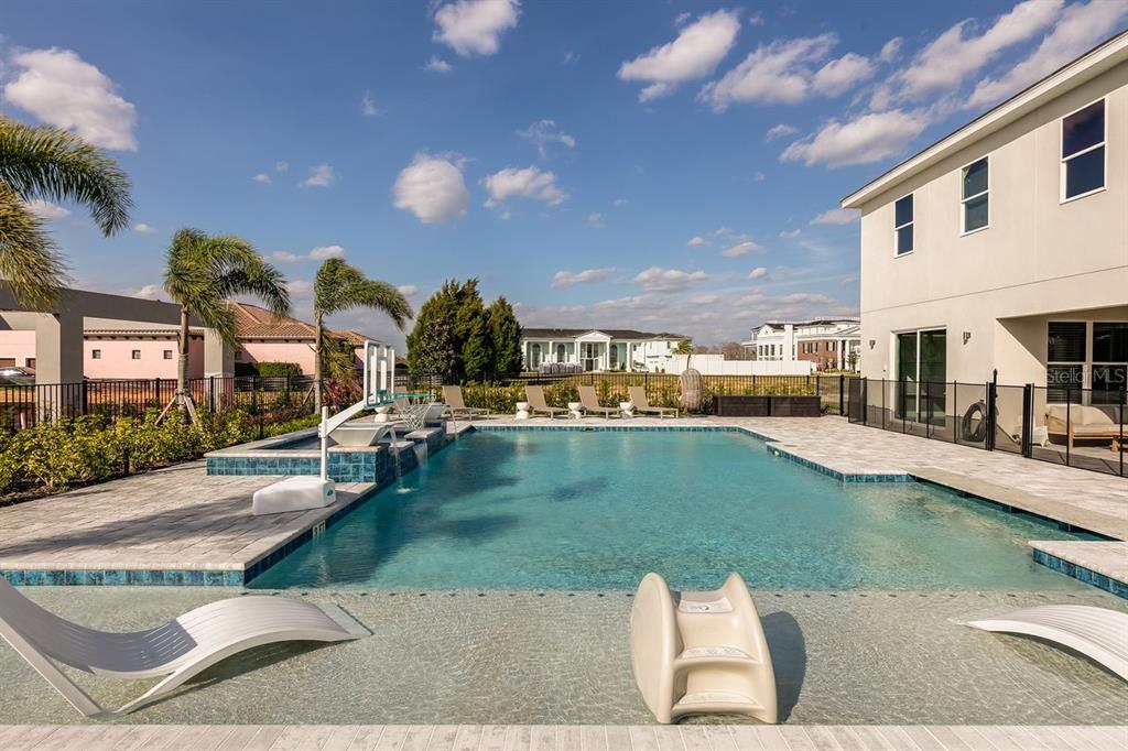 A backyard swimming pool with a sun shelf, slide, and basketball hoop next to a house — 1008 COYOTE CREEK WAY, REUNION, FL