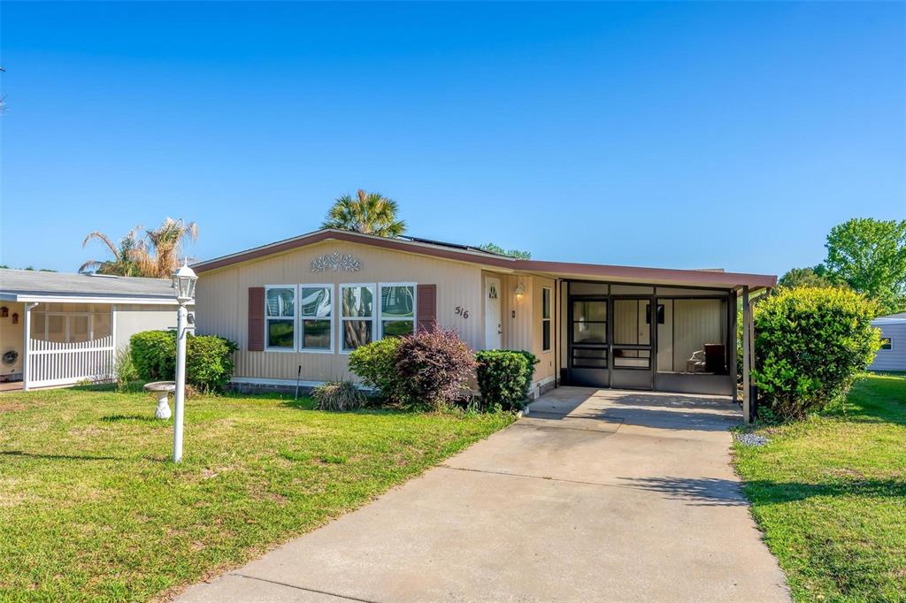 A single-story mobile home with a concrete driveway, carport, and front yard landscaping — 516 JASON DRIVE, LADY LAKE, FL