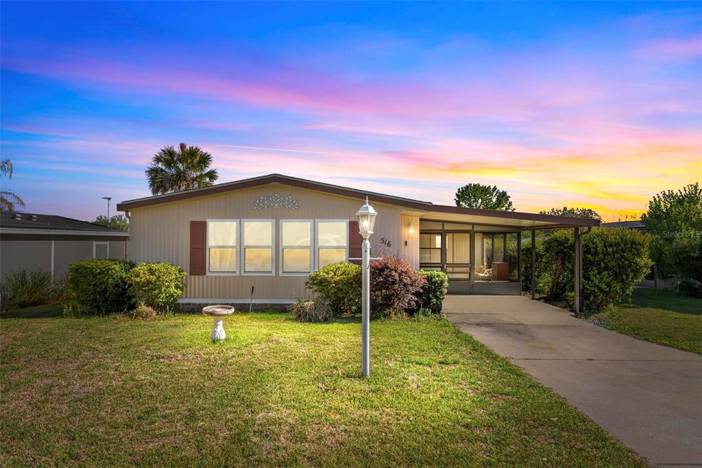 A single-story manufactured home features a tan exterior, a concrete driveway, and a screened porch — 516 JASON DRIVE, LADY LAKE, FL
