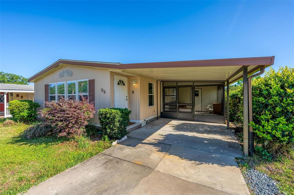 A single-story house with light-colored siding, a front carport, and a screened-in porch area — 516 JASON DRIVE, LADY LAKE, FL