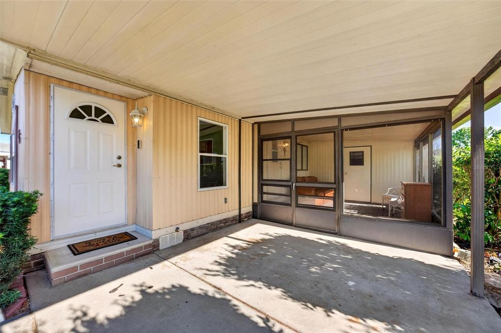 A covered concrete porch features a white front door and an adjacent screened-in patio area — 516 JASON DRIVE, LADY LAKE, FL