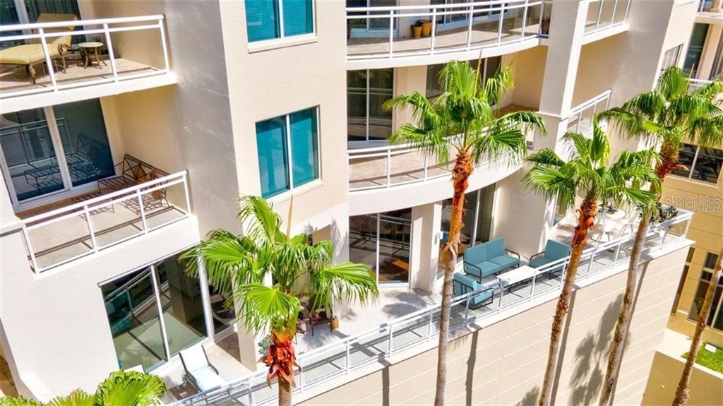 An elevated view of a multi-story building exterior featuring balconies with patio furniture and palm trees — 1300 BENJAMIN FRANKLIN DRIVE UNIT 301, SARASOTA, FL