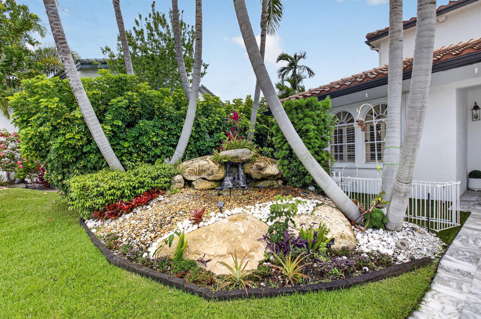 A landscaped front yard features a rock waterfall, palm trees, and a white house exterior — 1502 SW 5th Avenue, Boca Raton FL 33432, BOCA RATON, FL