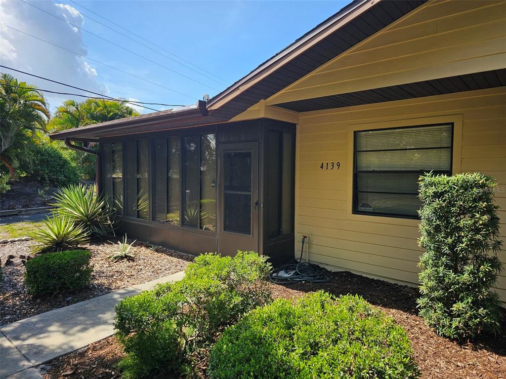 The exterior of a house features yellow siding, a screened-in porch, and a front walkway — 4139 66TH STREET CIRCLE W, BRADENTON, FL