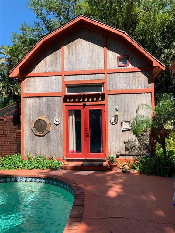 A wooden cabin with red trim and double glass doors sits beside a swimming pool — 1653 BRAVO DRIVE, CLEARWATER, FL