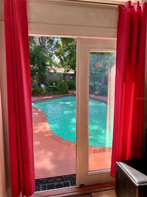 A view through a glass door shows a backyard swimming pool with a red deck — 1653 BRAVO DRIVE, CLEARWATER, FL