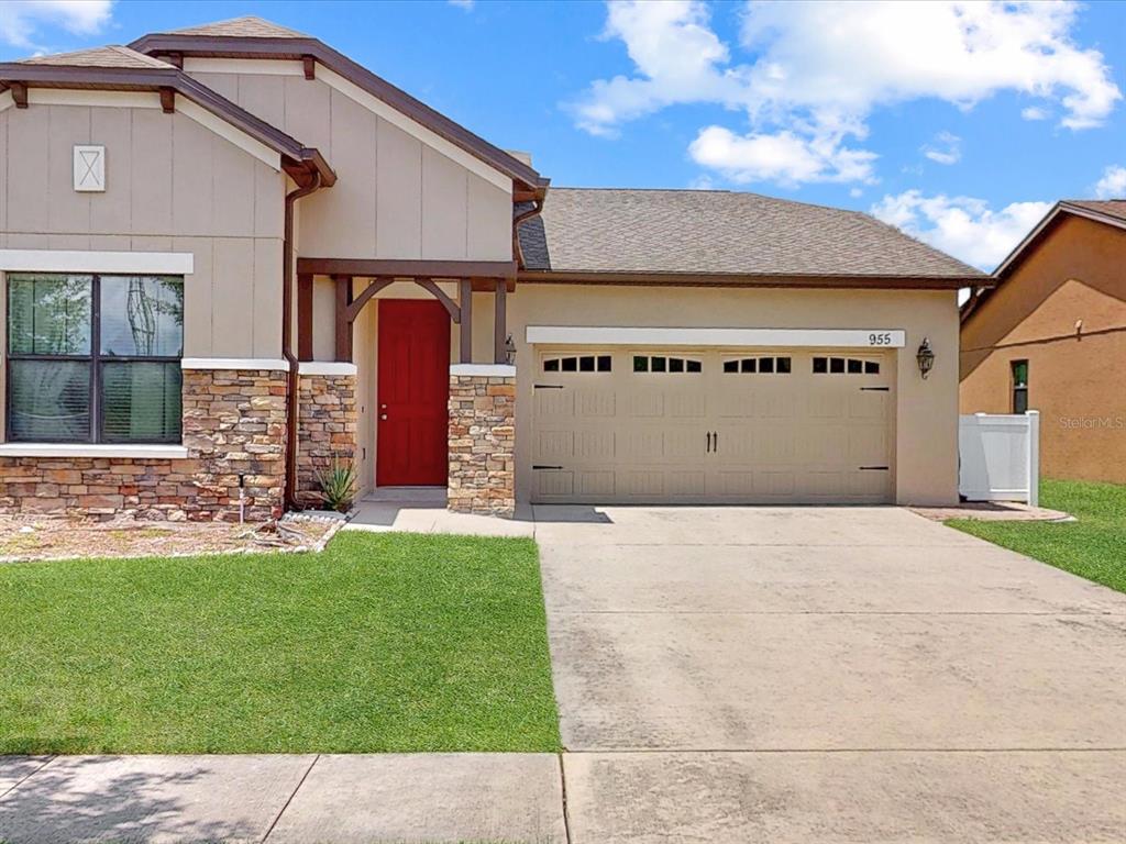 A single-story house with a red front door, stone accents, and a two-car garage — 955 LA MIRADA COURT, KISSIMMEE, FL