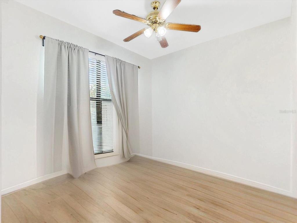 An empty bedroom features light wood-look flooring, white walls, a ceiling fan, and window curtains — 955 LA MIRADA COURT, KISSIMMEE, FL