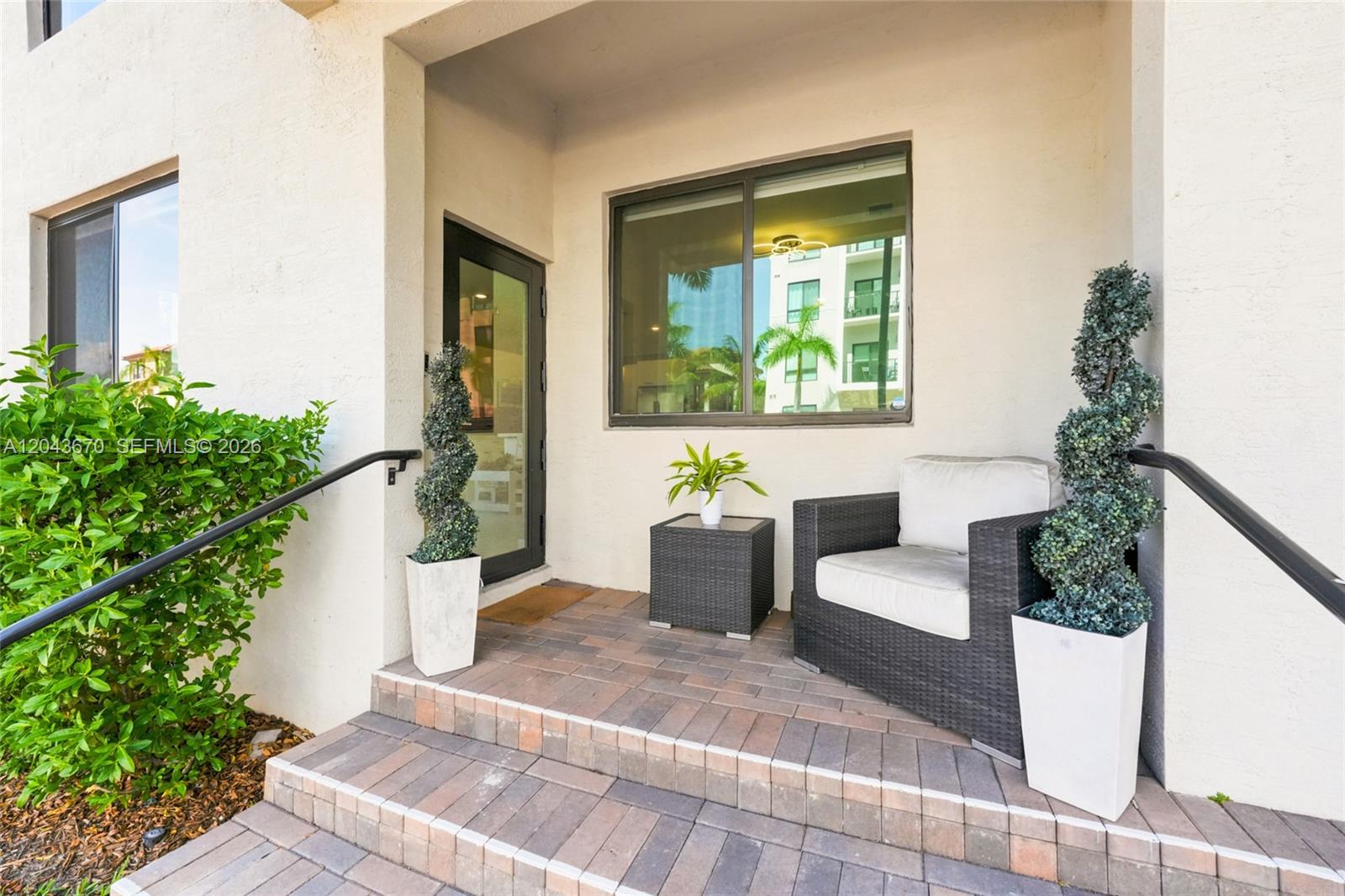 A paved entryway features a glass door, a wicker chair, and two potted topiary plants — 8167 NW 41st St # 101, Doral FL 33166, DORAL, FL