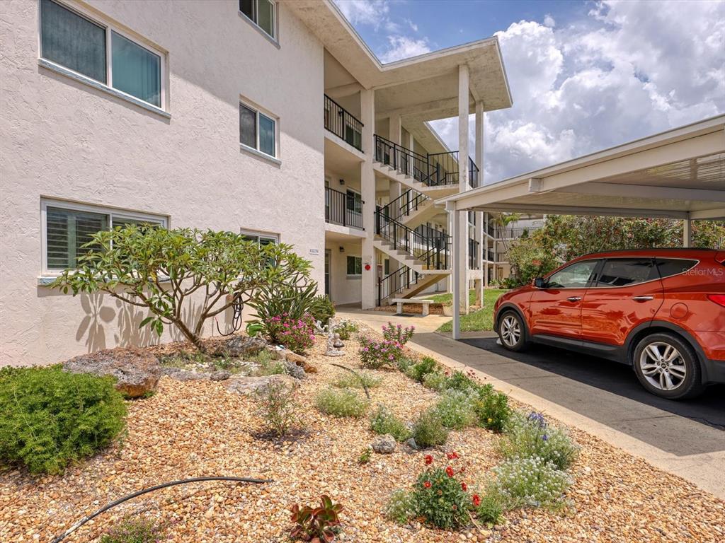 A multi-story apartment building exterior features an open staircase, landscaping, and a covered parking space — 708 TAMIAMI TRAIL S UNIT 105, VENICE, FL