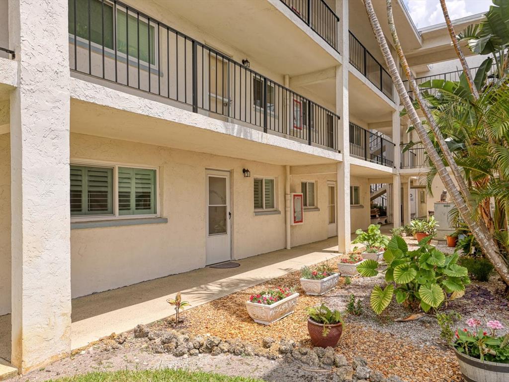 An exterior view of a multi-story apartment building with a walkway and potted plants — 708 TAMIAMI TRAIL S UNIT 105, VENICE, FL