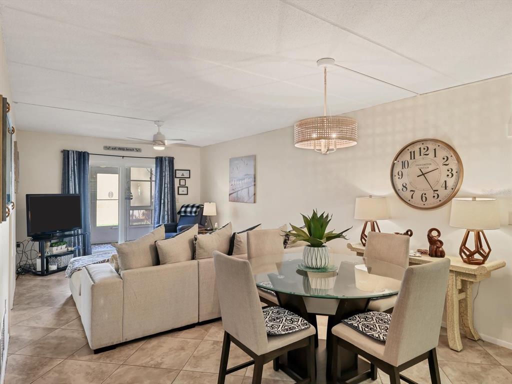 A living and dining area features a glass-top table, sectional sofa, and a large wall clock — 708 TAMIAMI TRAIL S UNIT 105, VENICE, FL