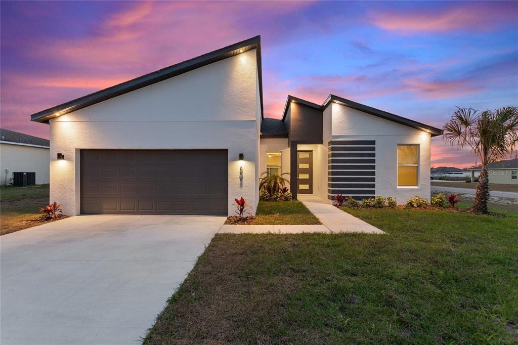 A modern single-story house with a white stucco exterior, a gray garage, and a sunset sky — 802 JAMES DRIVE, POINCIANA, FL