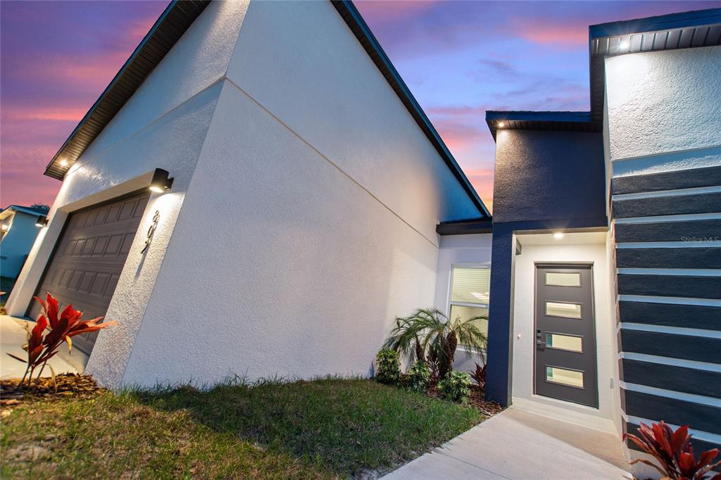 A modern house exterior features a white stucco wall, a gray garage door, and a front door — 802 JAMES DRIVE, POINCIANA, FL