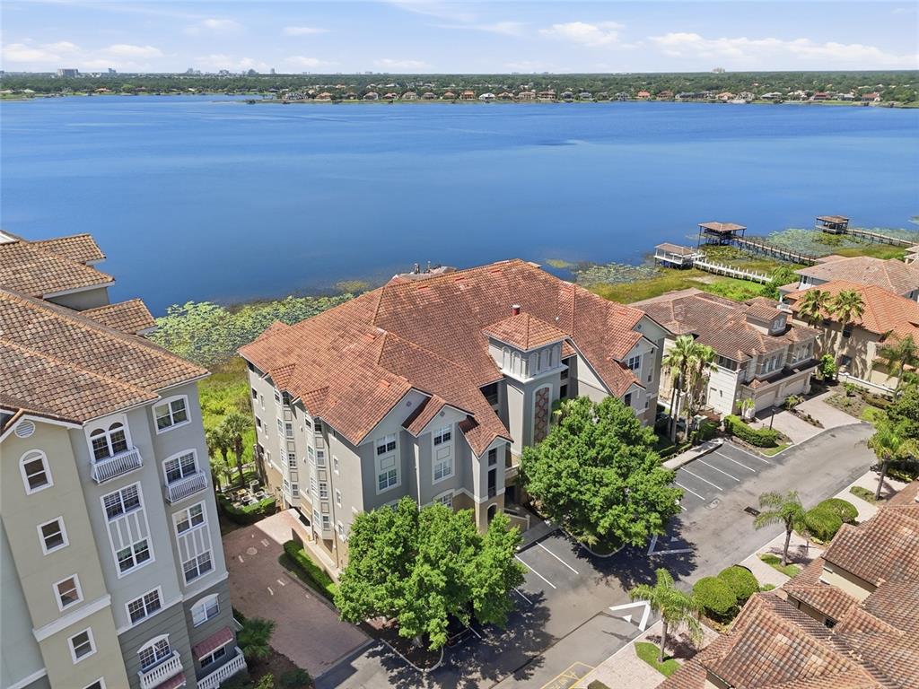 An aerial view shows multi-story apartment buildings with tile roofs situated beside a large lake — 8767 THE ESPLANADE UNIT 40, ORLANDO, FL
