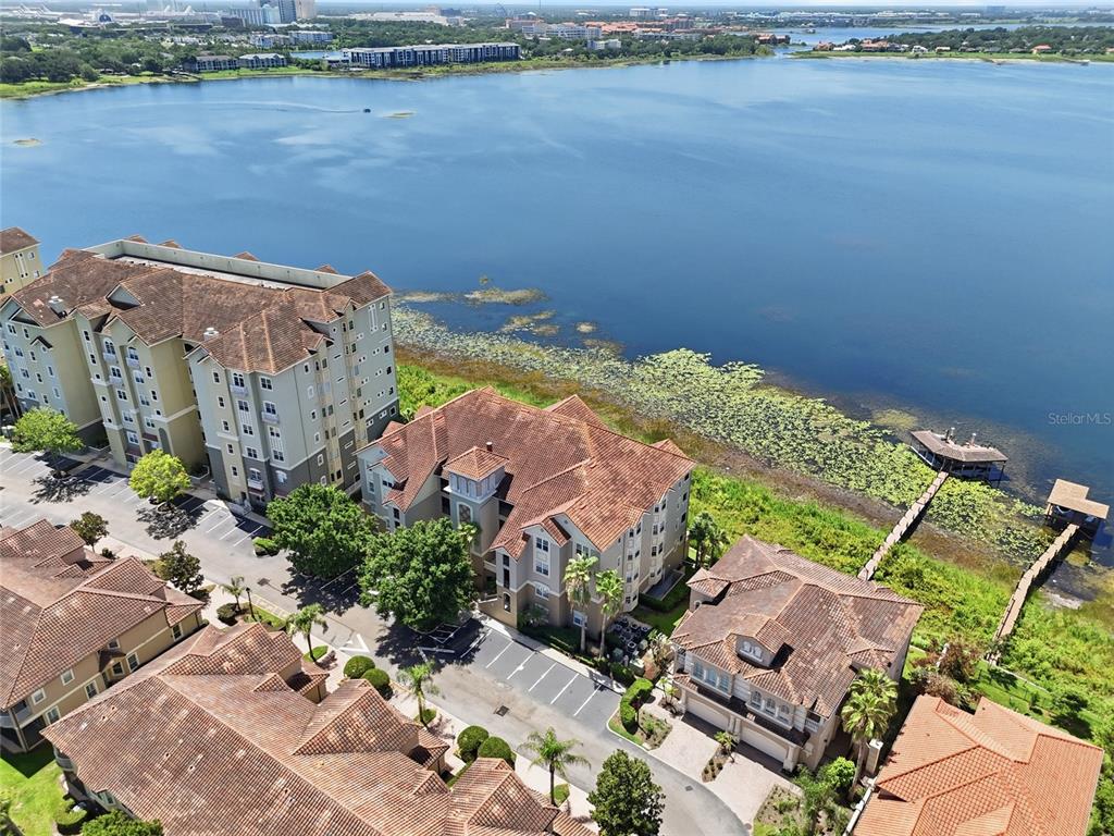 An aerial view shows several multi-story apartment buildings situated along the edge of a lake — 8767 THE ESPLANADE UNIT 40, ORLANDO, FL